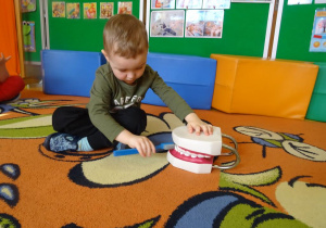Chłopiec prezentuje technikę mycia zębów z wykorzystaniem modelu szczęki.